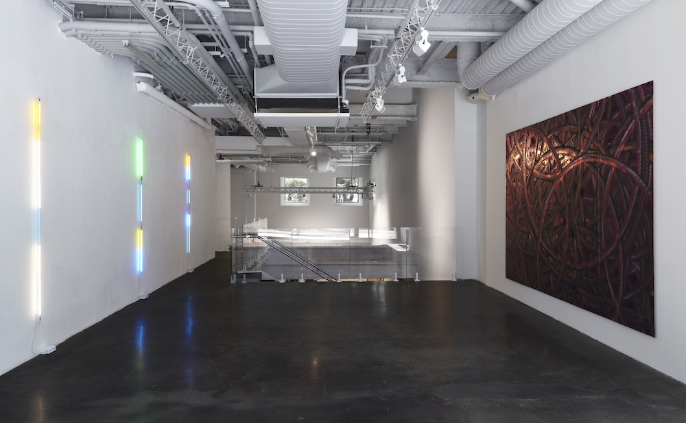 installation view of shady beautiful at malin gallery with three LED poles on one wall and on the other an abstract painting with swirls
